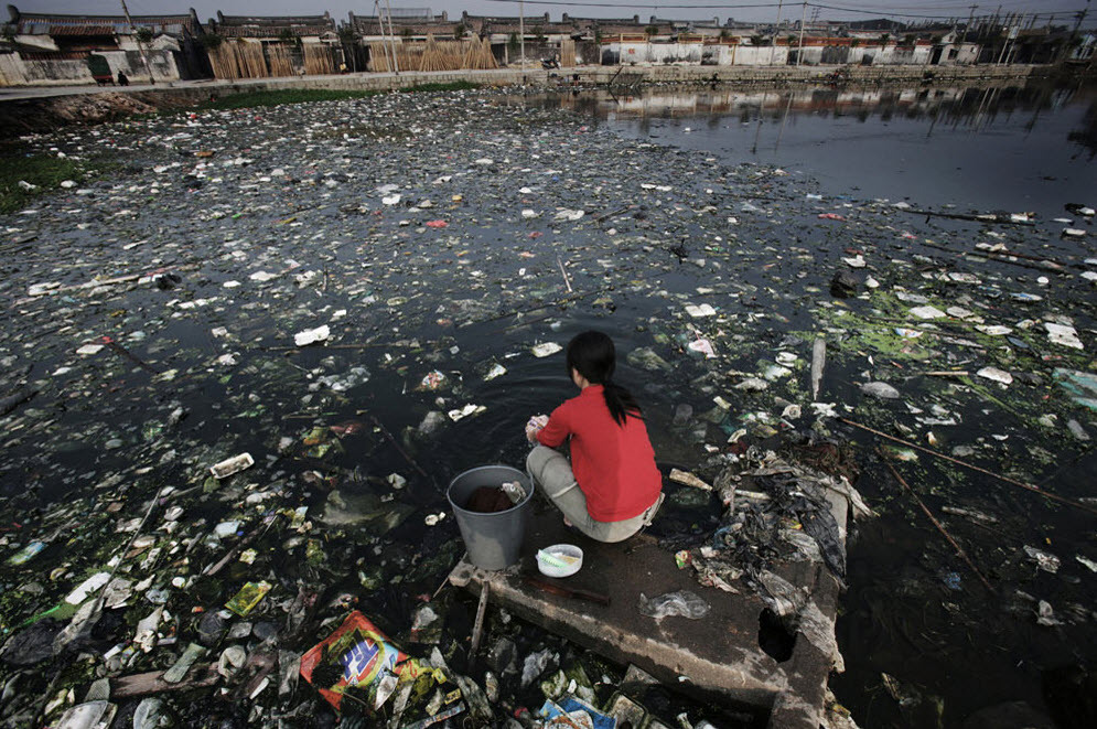 Une femme fait sa lessive dans un étang pollué